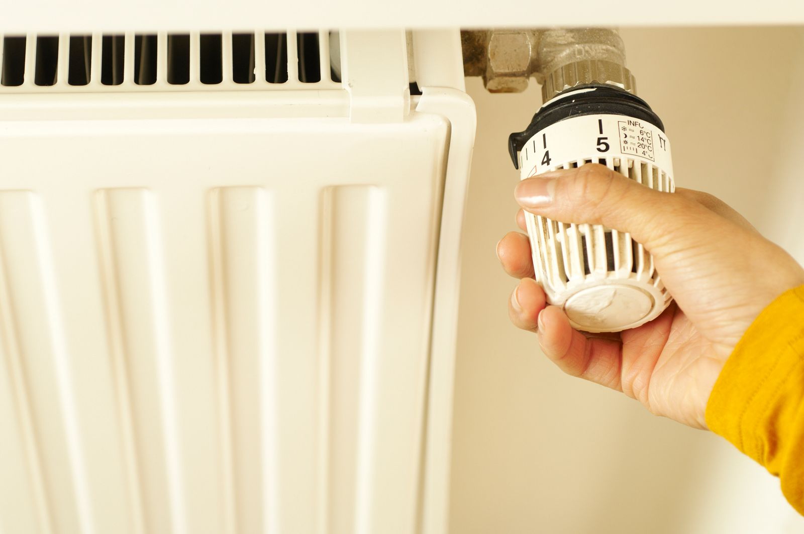 A hand turning the thermostatic valve on a white panel radiator