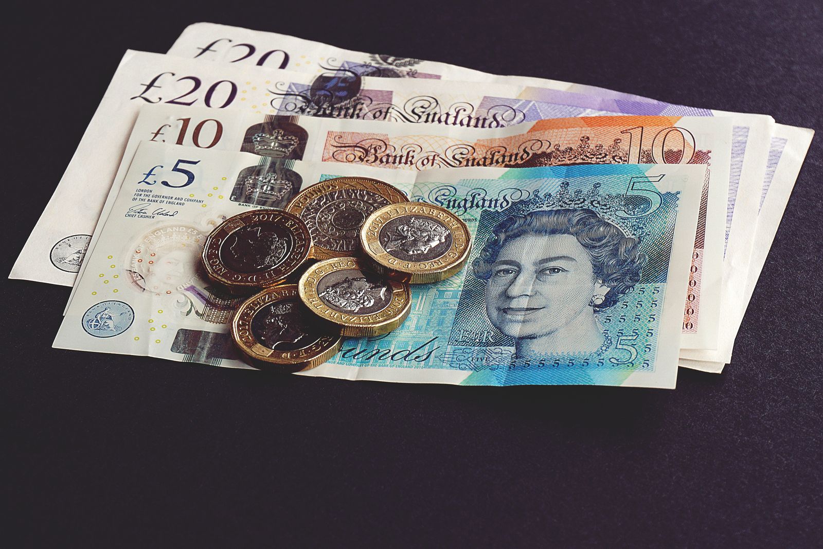 British banknotes fanned out with pound coins resting on top