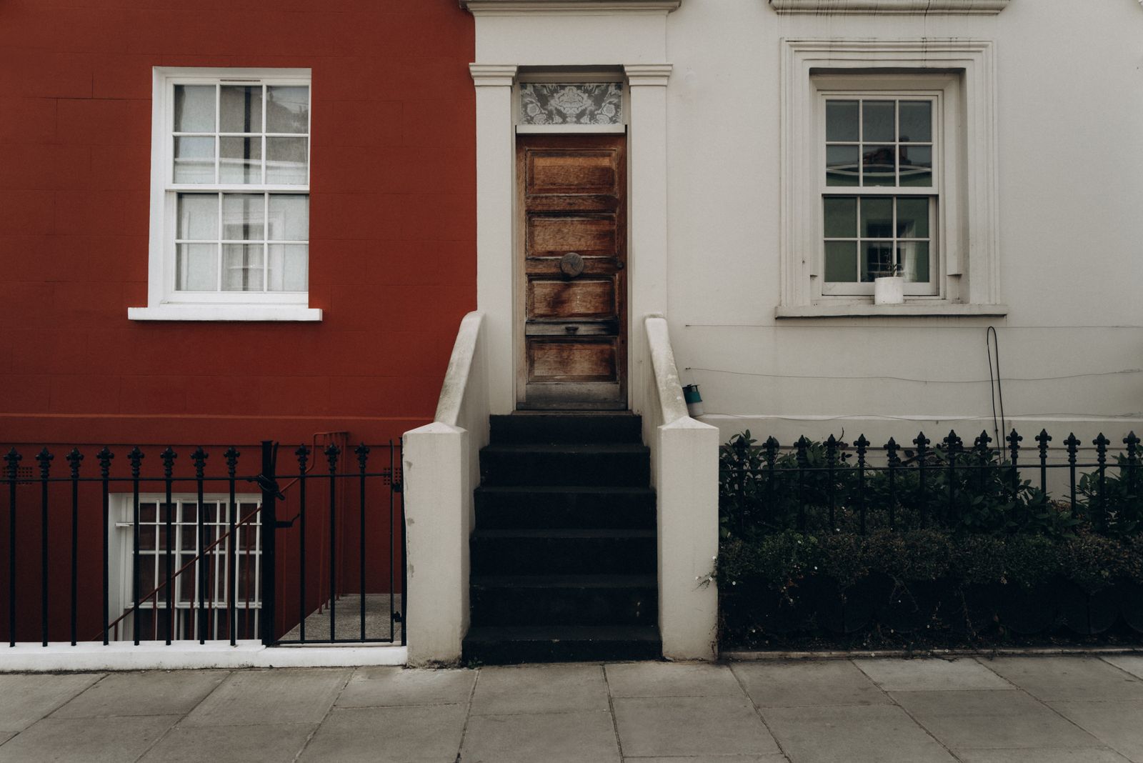 A panelled front door at the top of stone steps on a painted terrace, behind iron railings