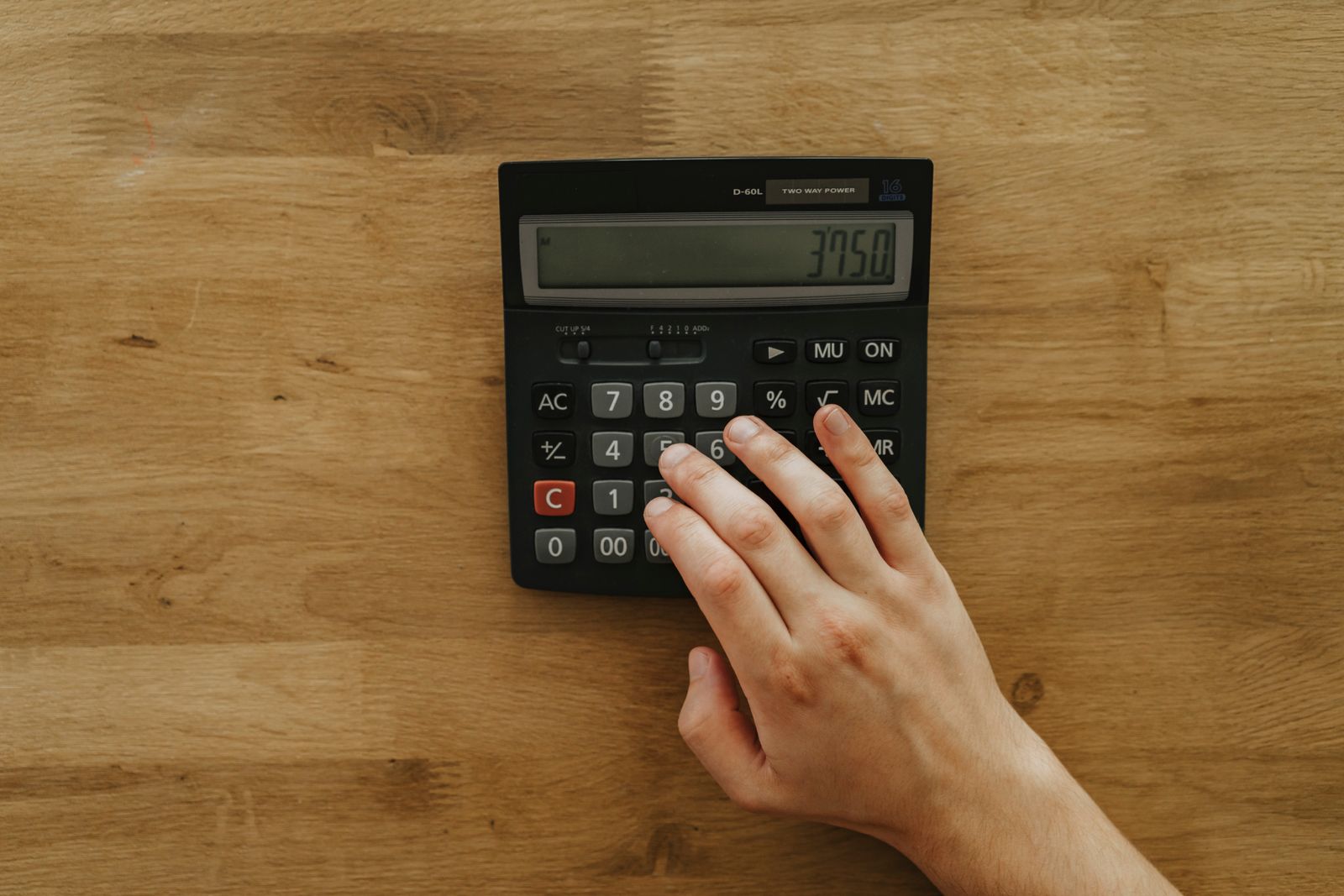 A hand using a calculator on a wooden desk