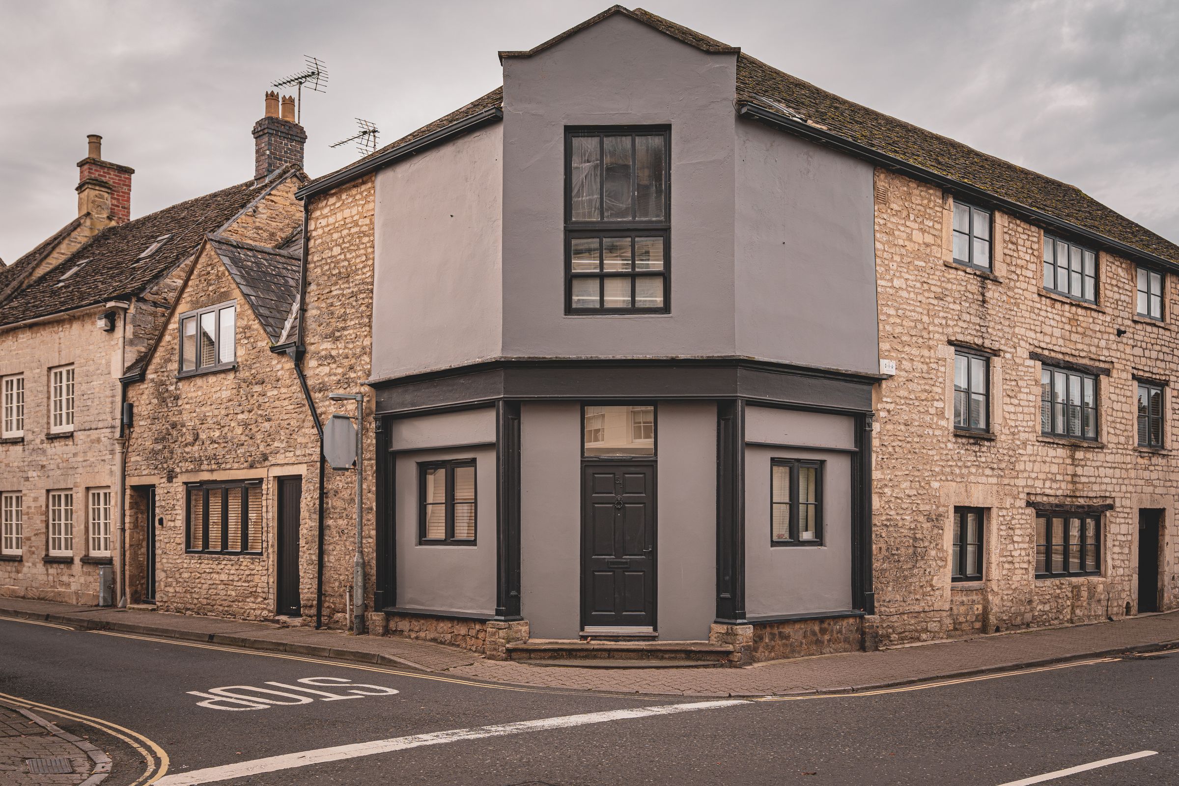 A stone-built corner property on an English street under an overcast sky