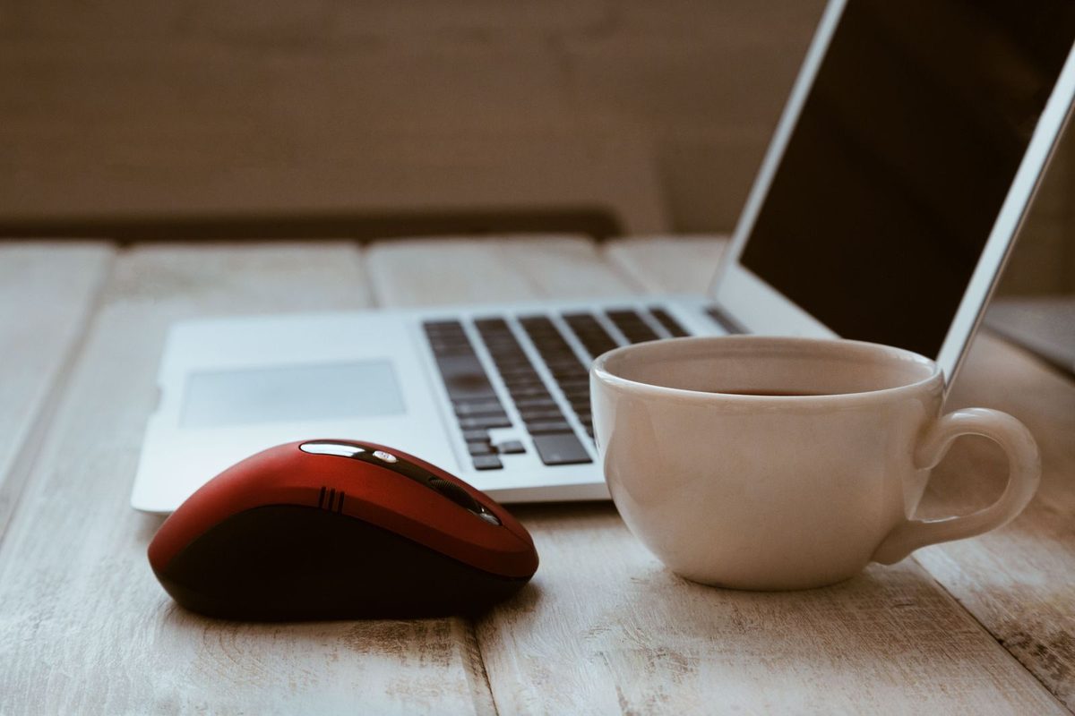 A laptop and mouse on a wooden desk beside a cup of tea