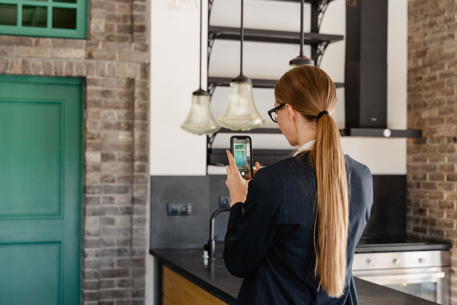 A person photographed from behind, taking a photo of a kitchen on their phone