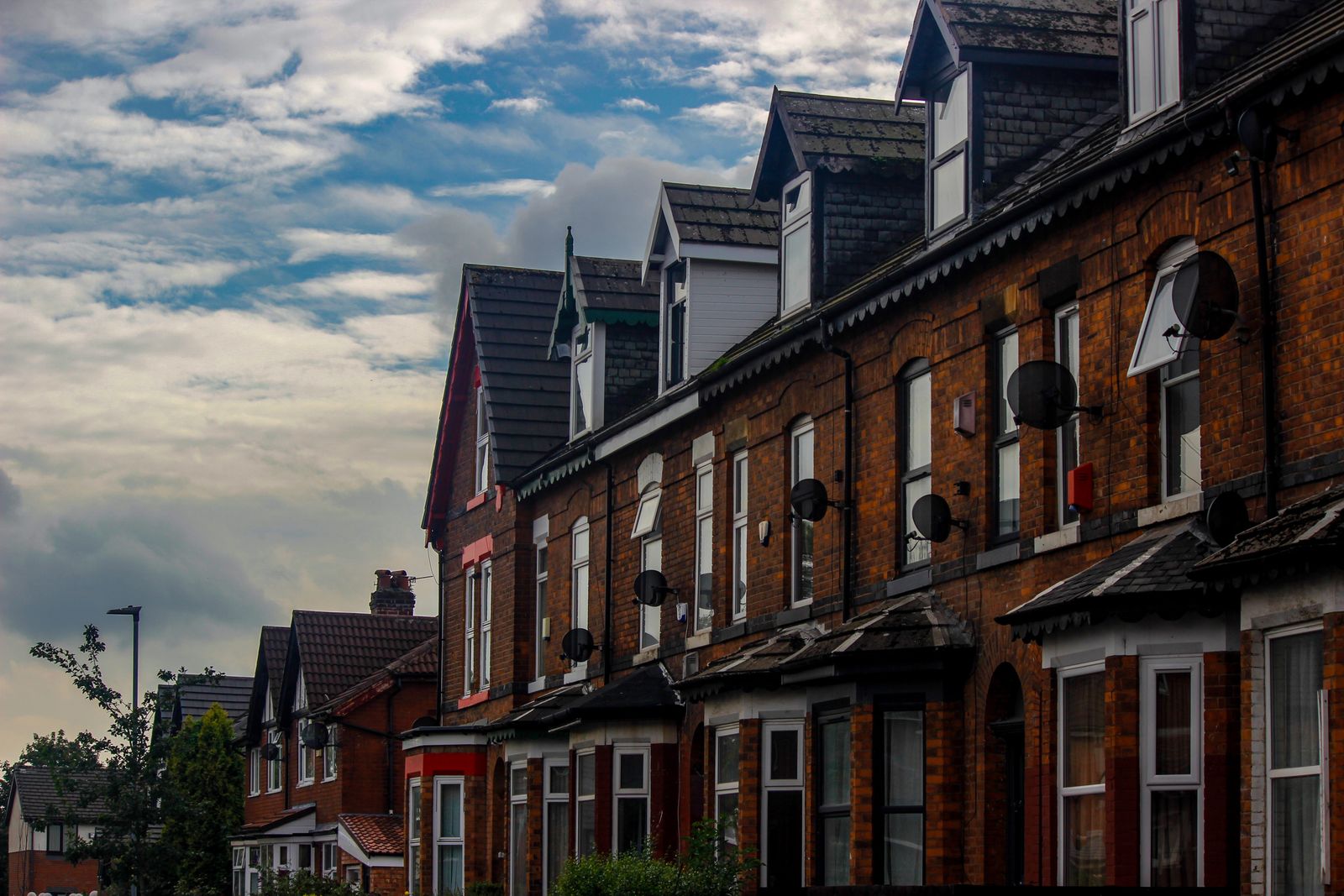 A row of red-brick terraced houses with dormer loft conversions, seen from below against a cloudy sky