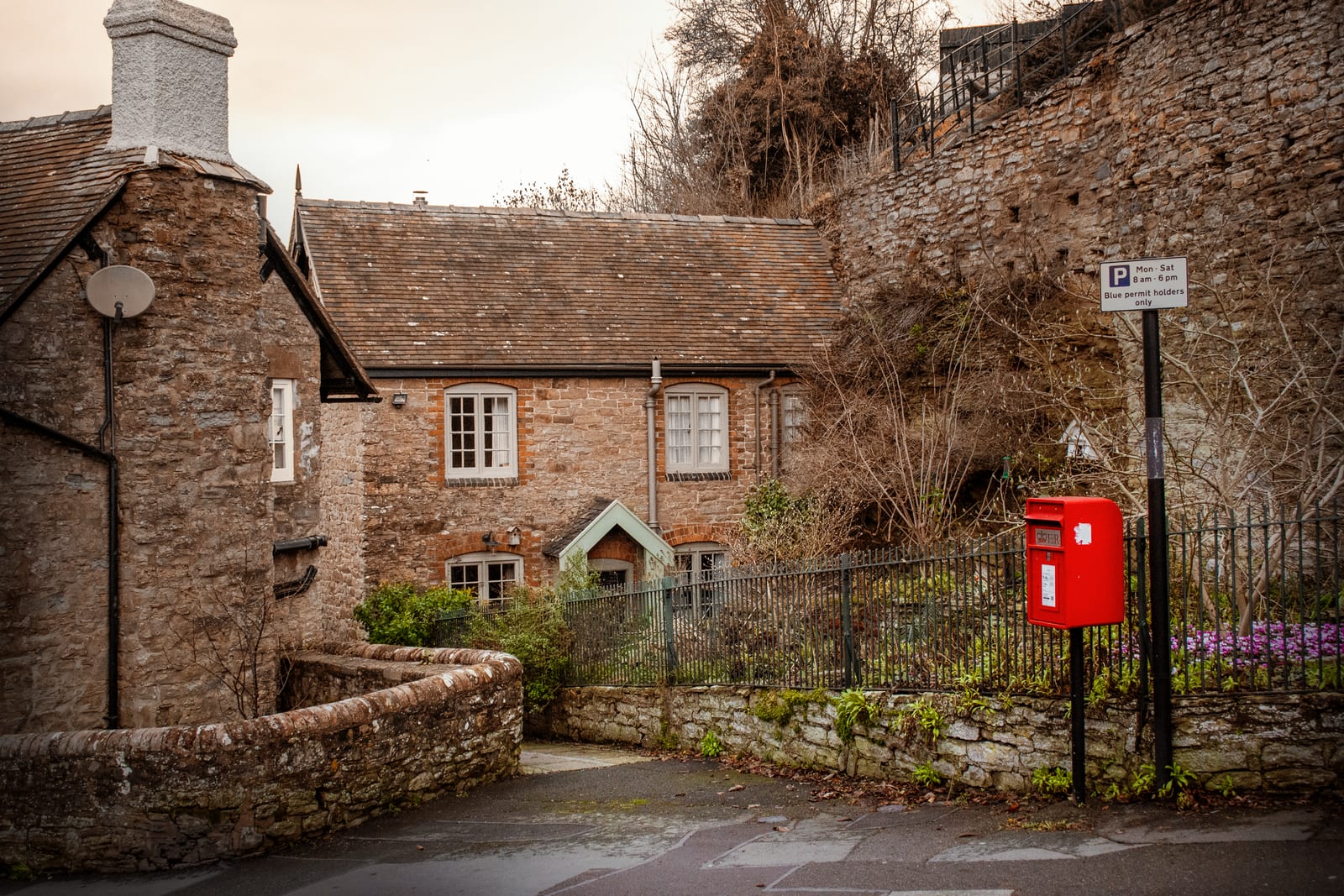 A stone cottage with a tiled roof on a village lane, a red pillar box at the kerb