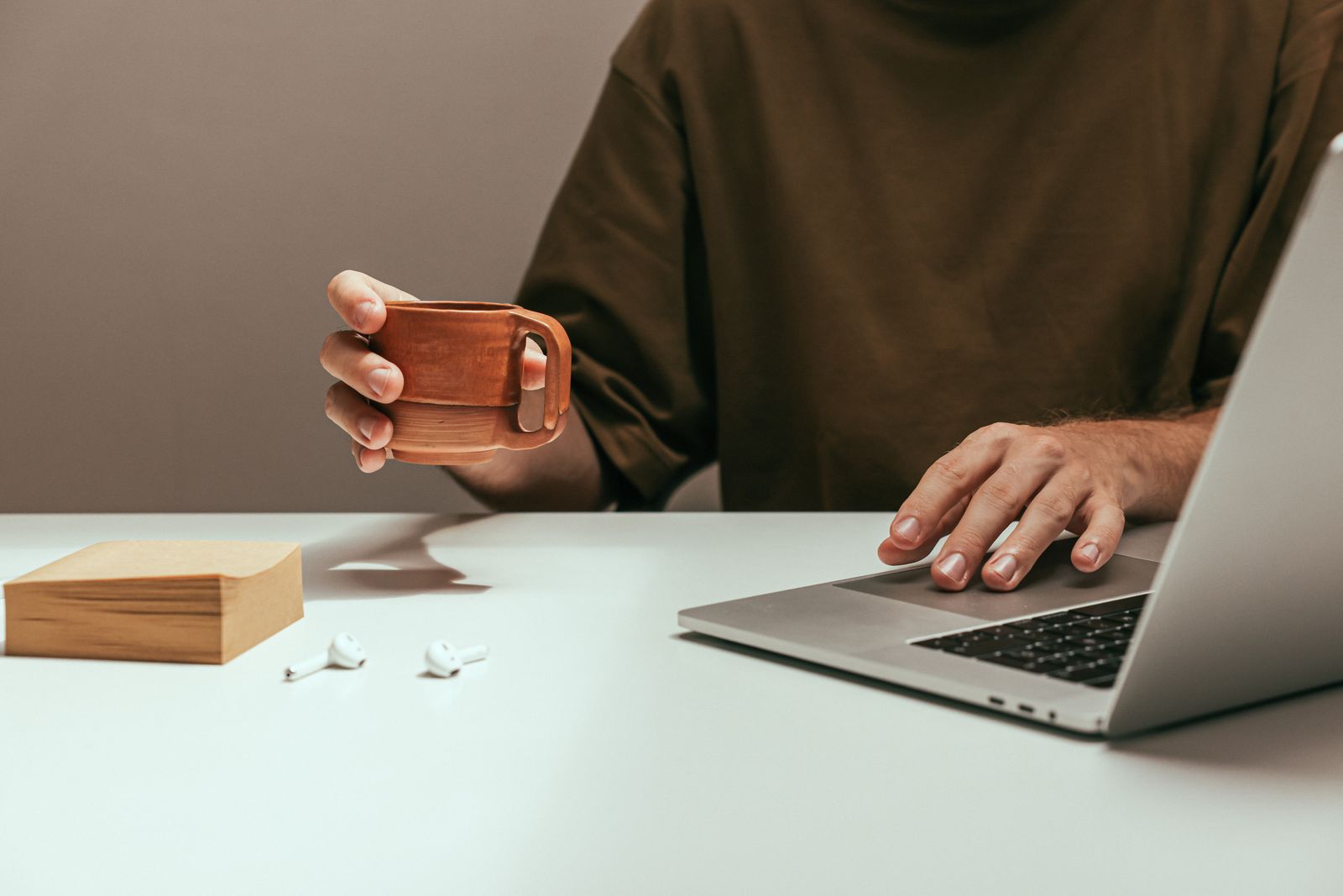A person working at a laptop on a pale desk, holding a mug